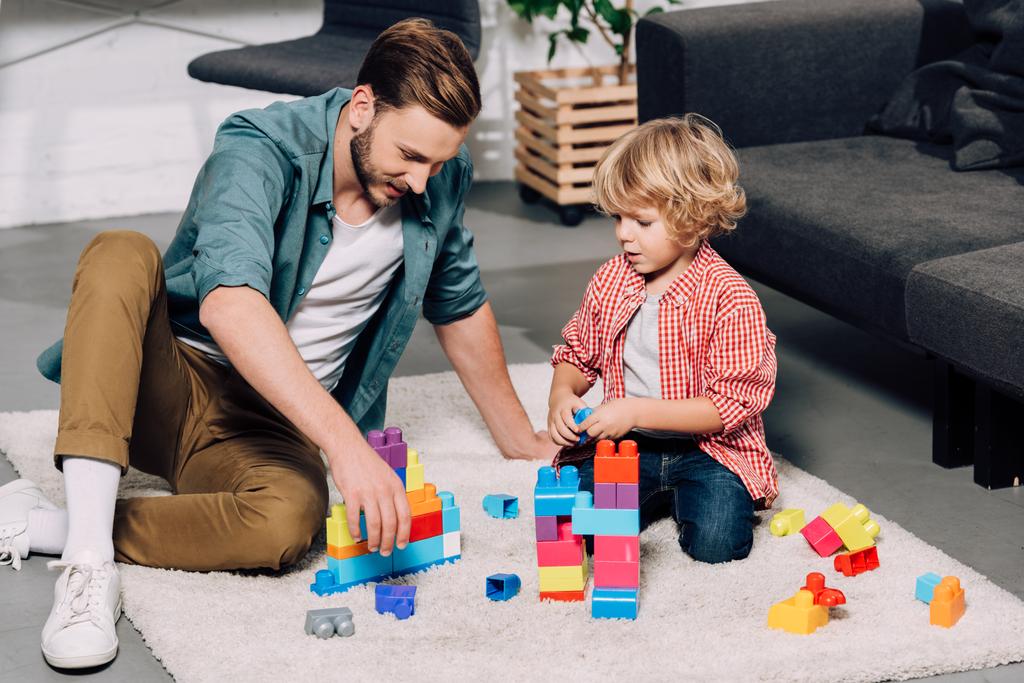 ο άνθρωπος με το μικρό γιο παίζοντας με πολύχρωμο πλαστικό μπλοκ στο πάτωμα στο σπίτι - Φωτογραφία, εικόνα