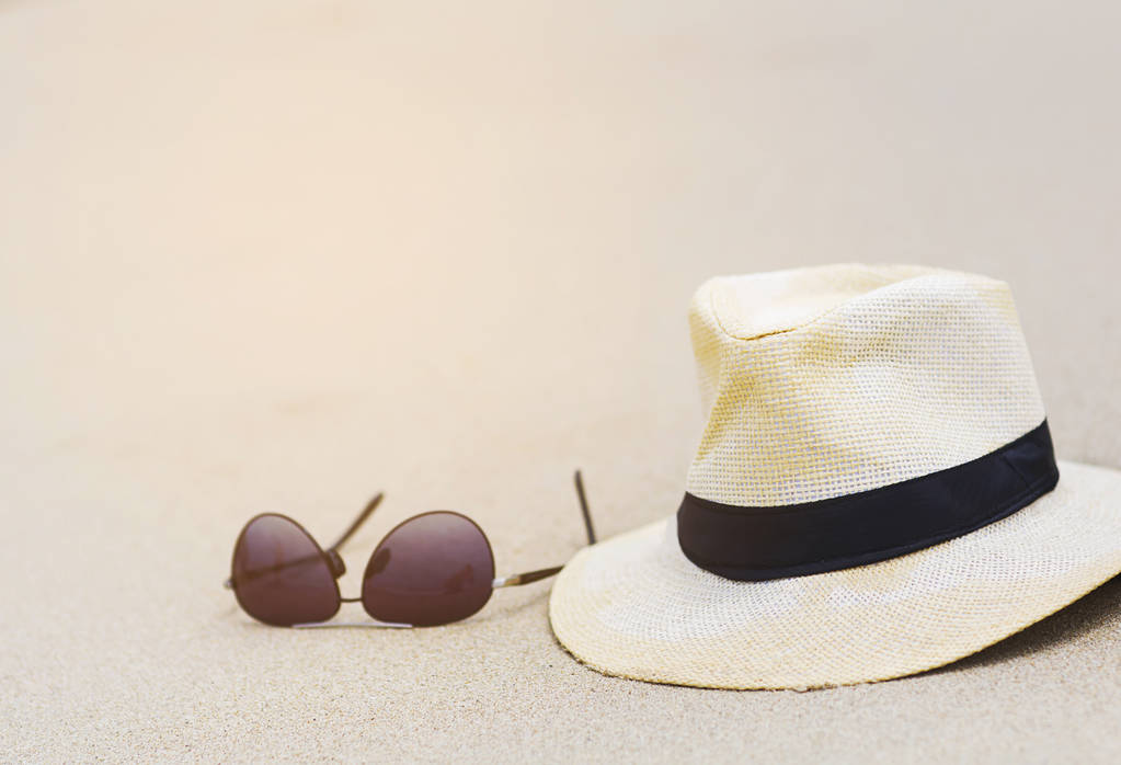 Hoed en zonnebril op het strand van fijn zand in zonnige dag - Foto, afbeelding