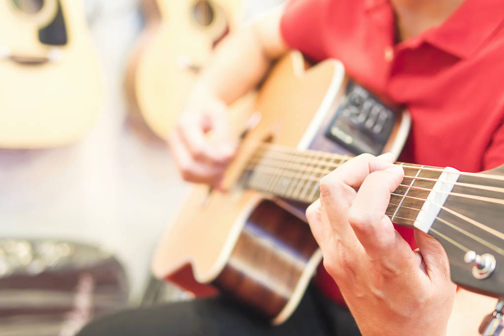 Άντρας παίζει κιθάρα με αναρτημένα κιθάρες φόντο - Φωτογραφία, εικόνα