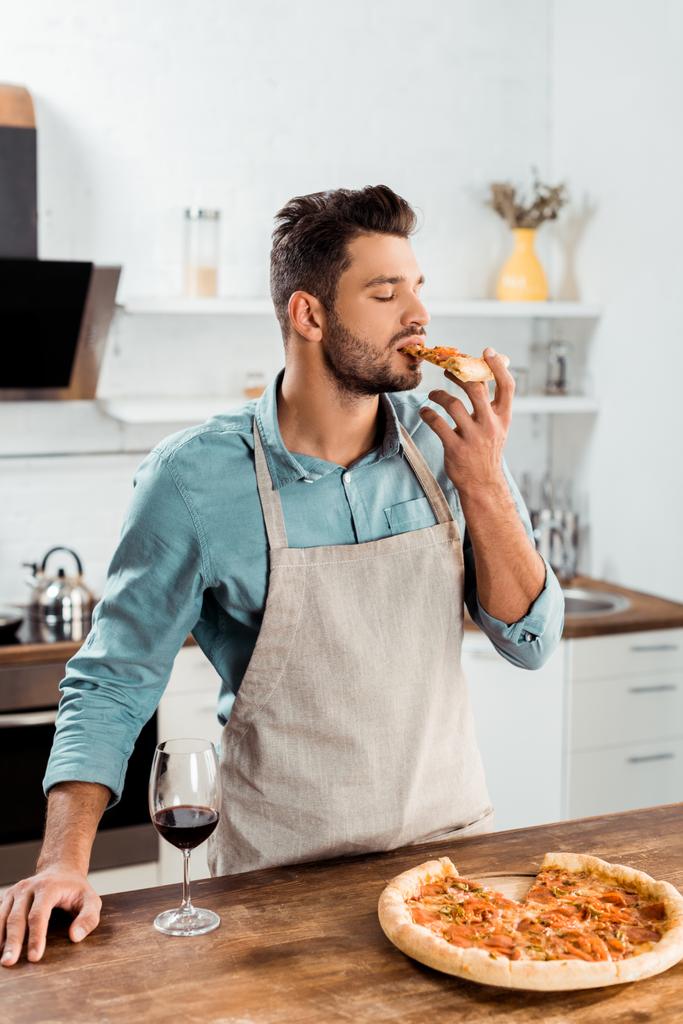 fiatal férfi-kötény, házi készítésű pizzát eszik a konyhában - Fotó, kép