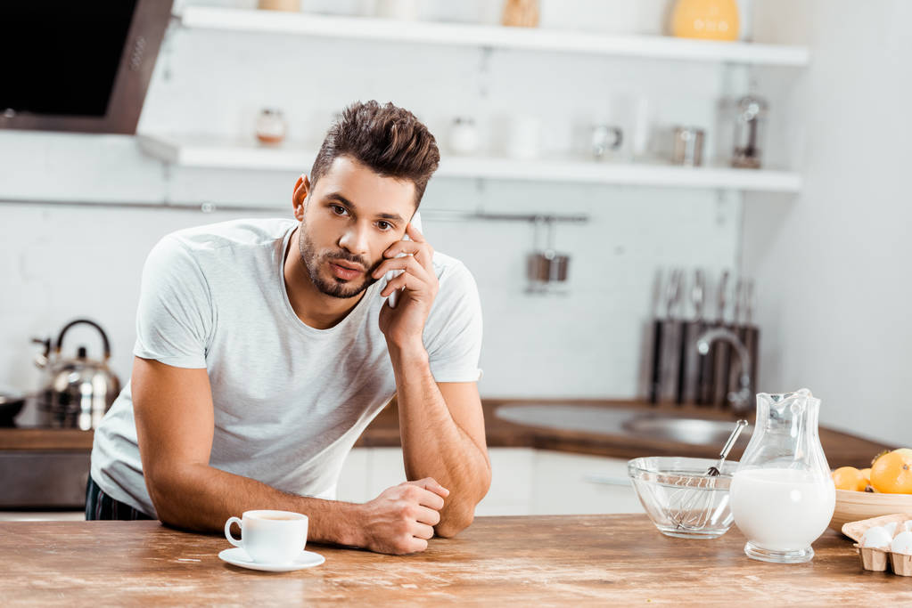 mladý muž se v kuchyni u stolu a mluví o smartphone na ranní - Fotografie, Obrázek