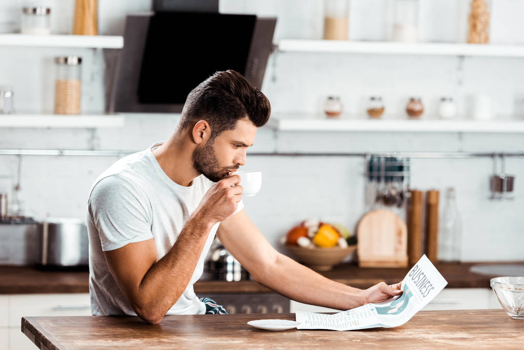 joven enfocado beber café y leer el periódico en la cocina por la mañana
 - Foto, imagen