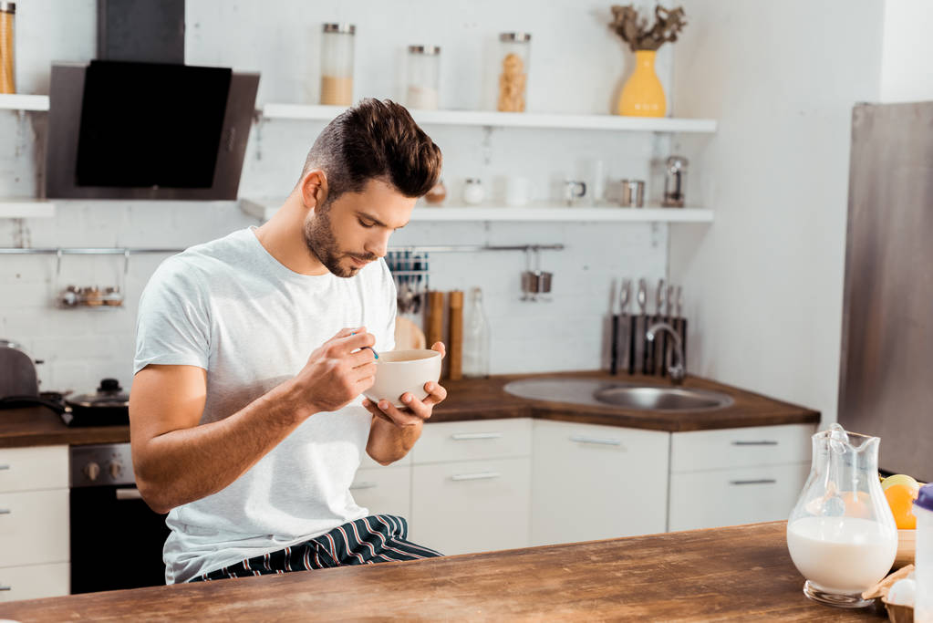 jonge man in pyjama cornflakes te eten voor het ontbijt thuis - Foto, afbeelding