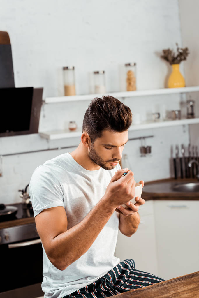Blick aus der Vogelperspektive auf einen jungen Mann im Pyjama, der zu Hause Müsli zum Frühstück isst - Foto, Bild