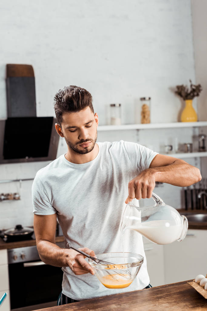 jonge man gieten melk en koken omelet op ochtend - Foto, afbeelding