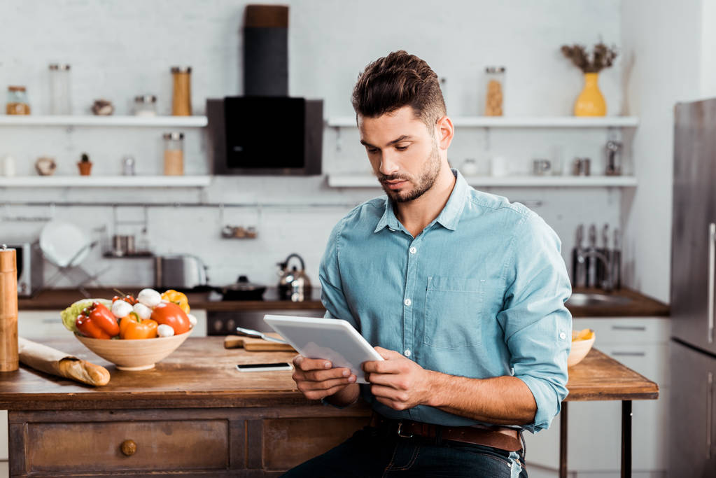 handsome young man using digital tablet while cooking in kitchen - Photo, Image