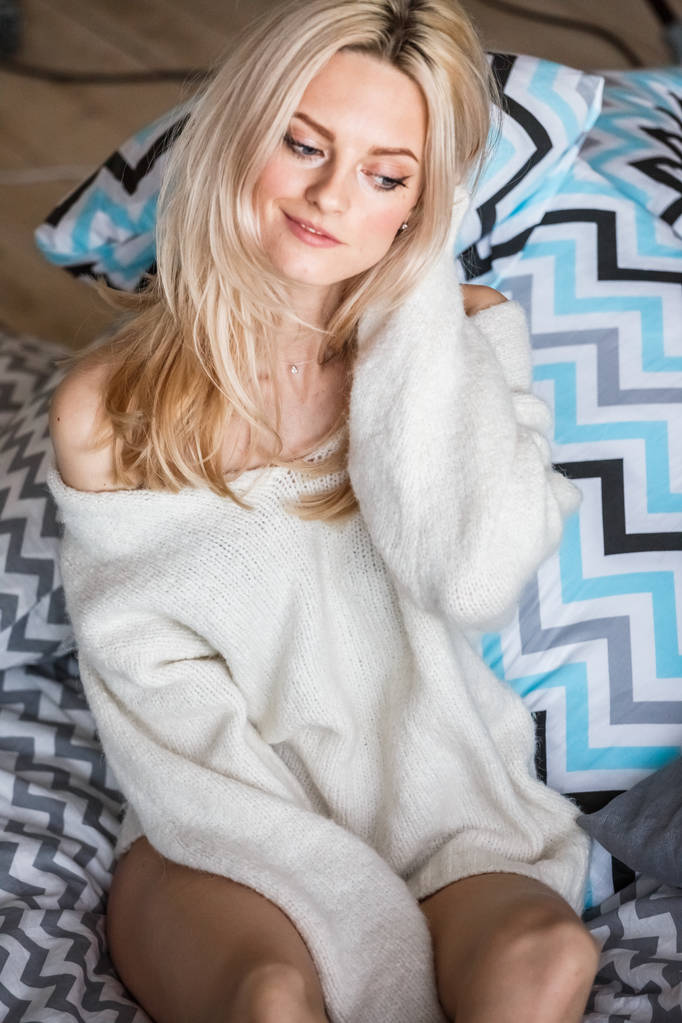 Studio portret van schoonheid blonde vrouw dragen witte trui. Vrouwelijk model met stijlvolle make-up liggend in bed - Foto, afbeelding