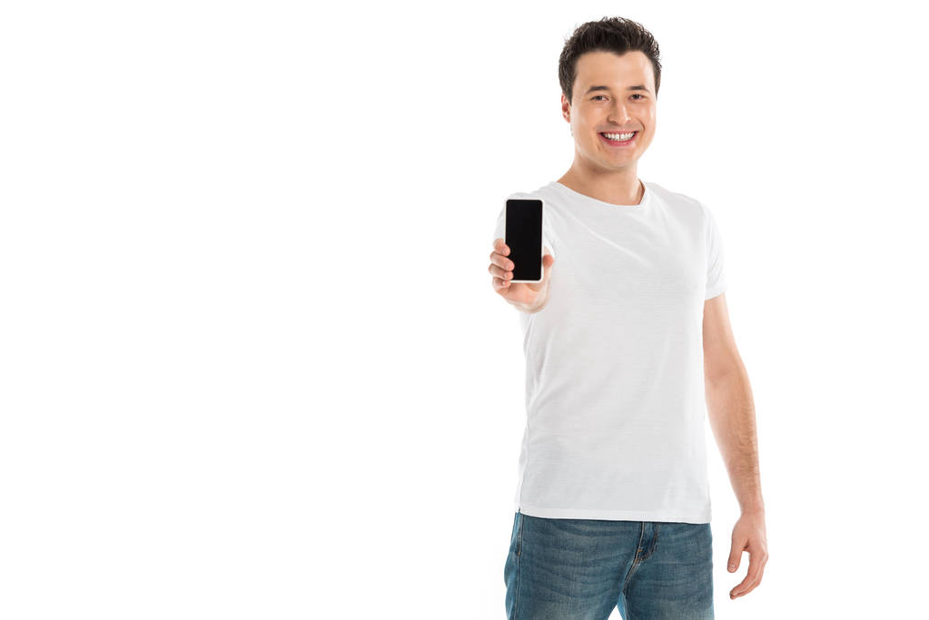 pohledný muž představí smartphone s prázdnou obrazovkou a při pohledu na fotoaparát izolované na bílém - Fotografie, Obrázek