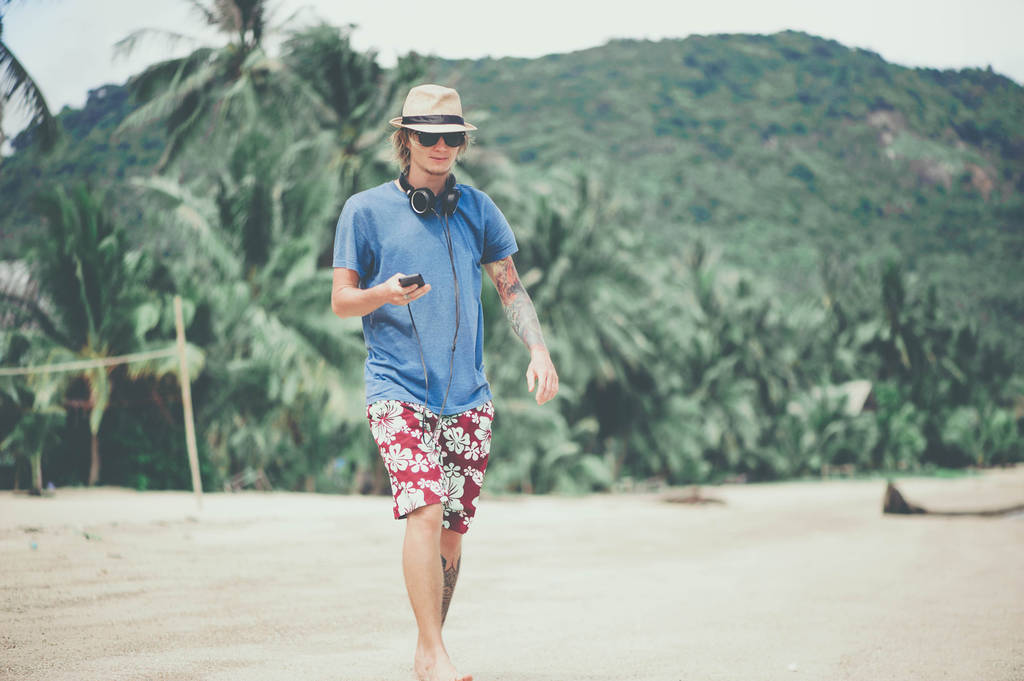 junger Mann mit Kopfhörern und Sonnenbrille am Strand spazieren gehen und Musik hören - Foto, Bild
