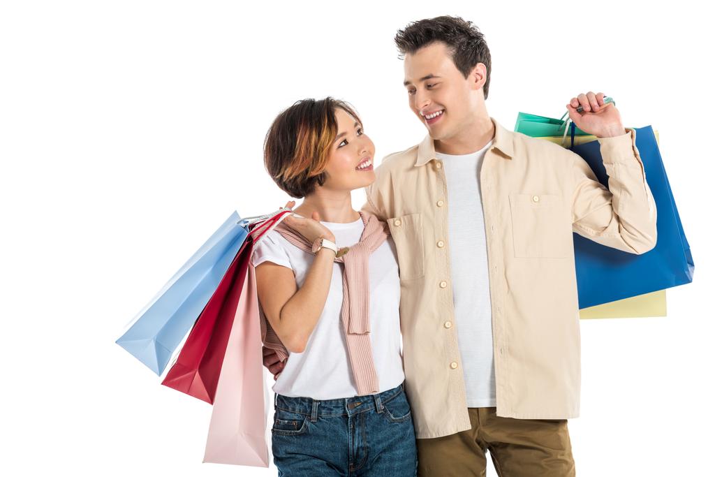 smiling couple looking at each other and carrying shopping bags isolated on white  - Photo, Image