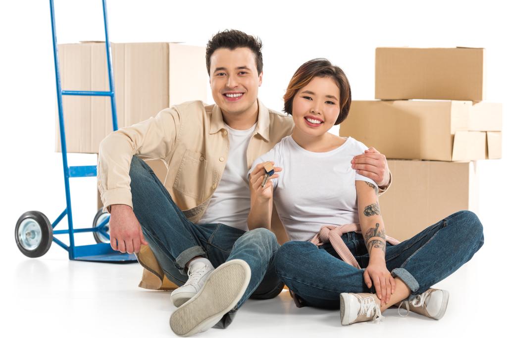 Paar umarmt und hält Schlüssel mit Pappkartons im Hintergrund, Umzug in neues Hauskonzept - Foto, Bild