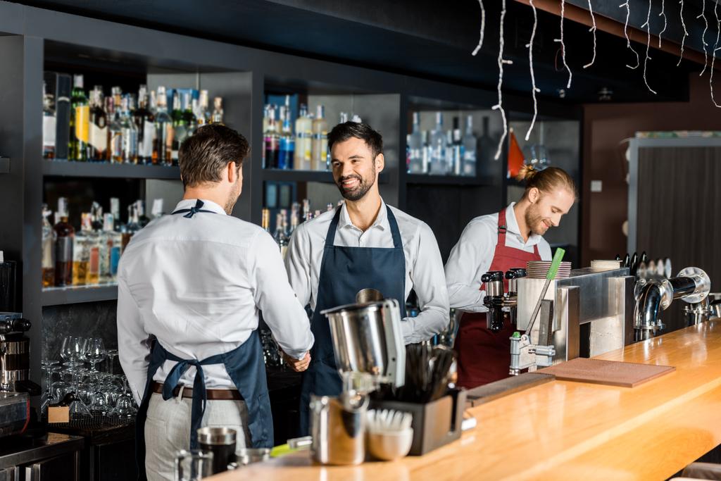 adult barmen in aprons shaking hands near counter - Photo, Image