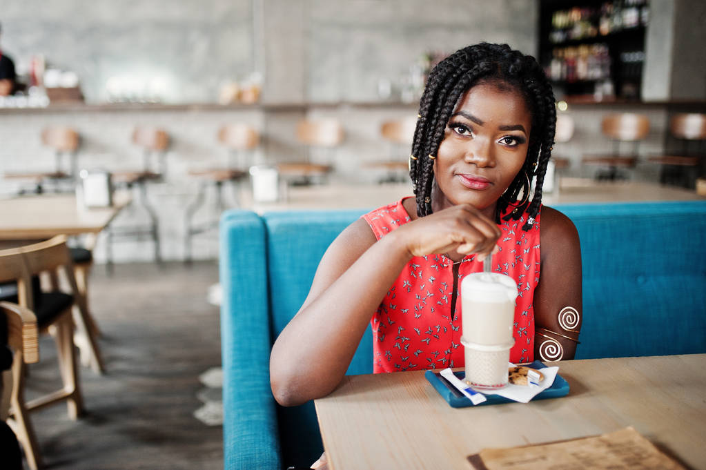 Atrakcyjne african american kobieta siedzi przy stole w kawiarni z latte. - Zdjęcie, obraz