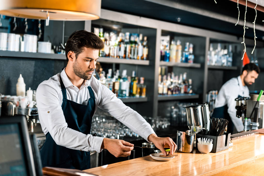 handsome barista putting sugar sticks and spoon on saucer at counter - Photo, Image