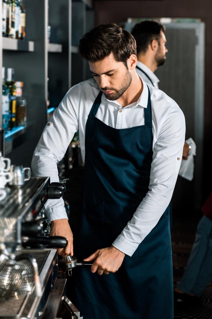 όμορφος barista στην ποδιά χρησιμοποιώντας μηχανή του καφέ στο χώρο εργασίας - Φωτογραφία, εικόνα