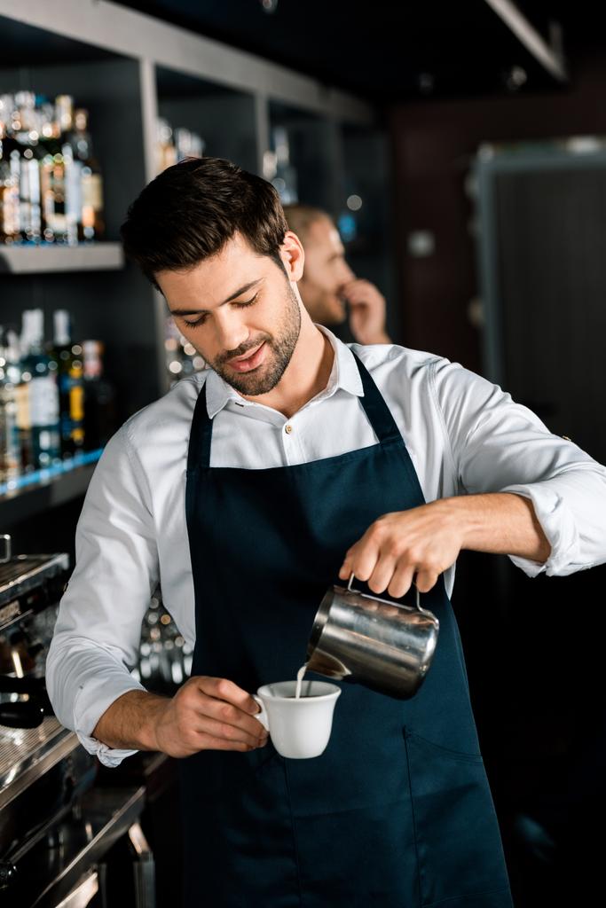 handsome barista in apron pouring milk from jar at workplace - Photo, Image