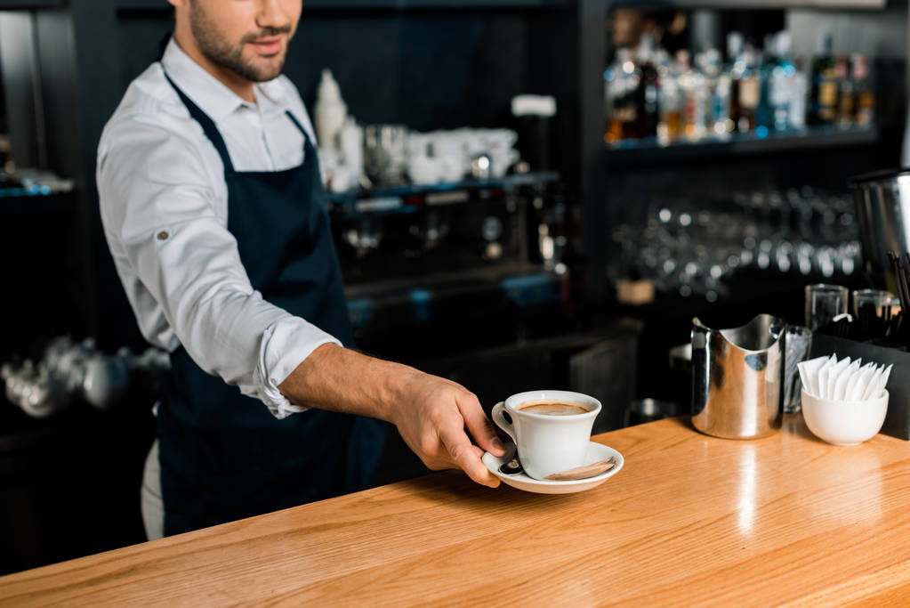 vista ritagliata di barista in grembiule mettendo tazza di caffè al bancone di legno
 - Foto, immagini
