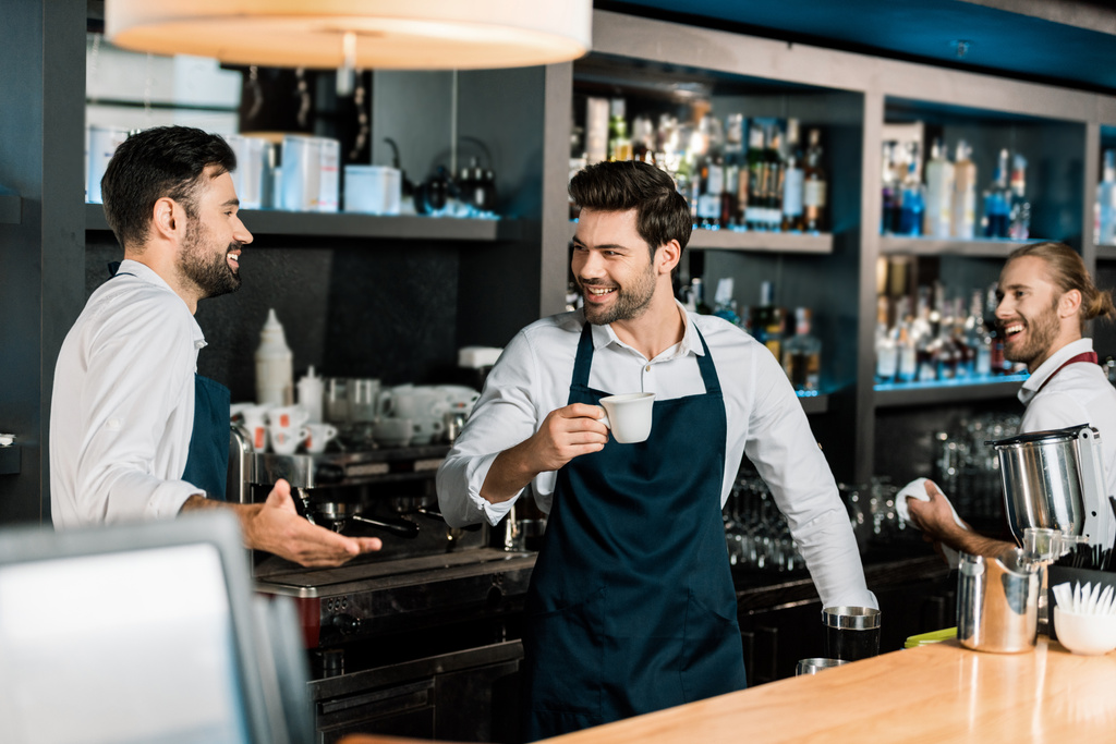 guapo barman alegre beber café y hablar con colegas en el lugar de trabajo
 - Foto, imagen