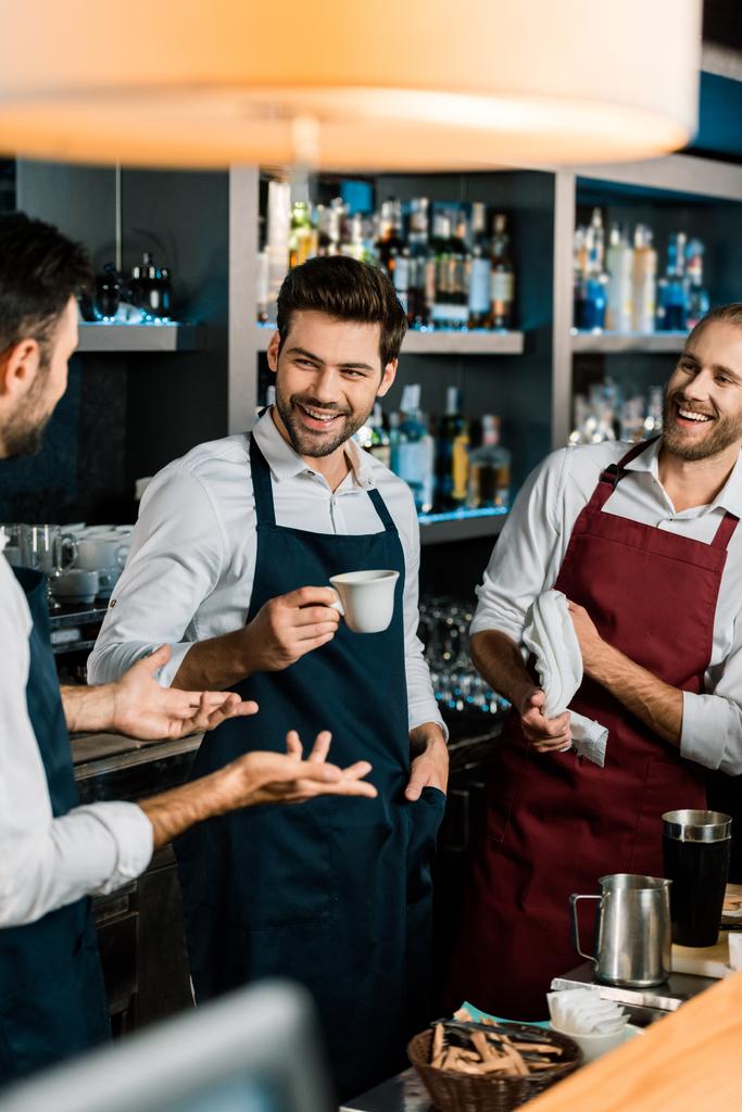 smiling barman drinking coffee and talking to colleagues at workplace - Photo, Image