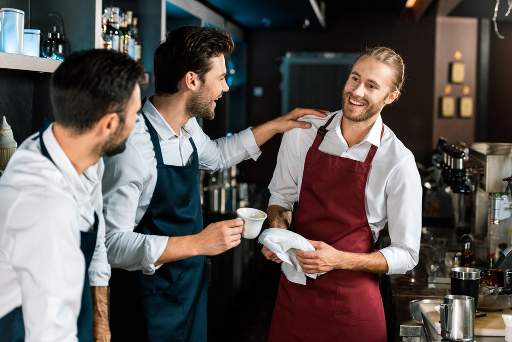 smiling barman drinking coffee and talking to colleagues at workplace - Photo, Image