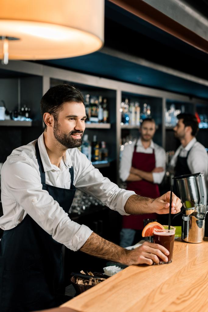 cheerful bartender putting straw in cocktail at wooden counter - Photo, Image