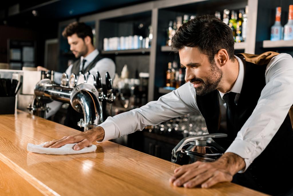Barman cleaning wooden counter with white cloth  - Photo, Image