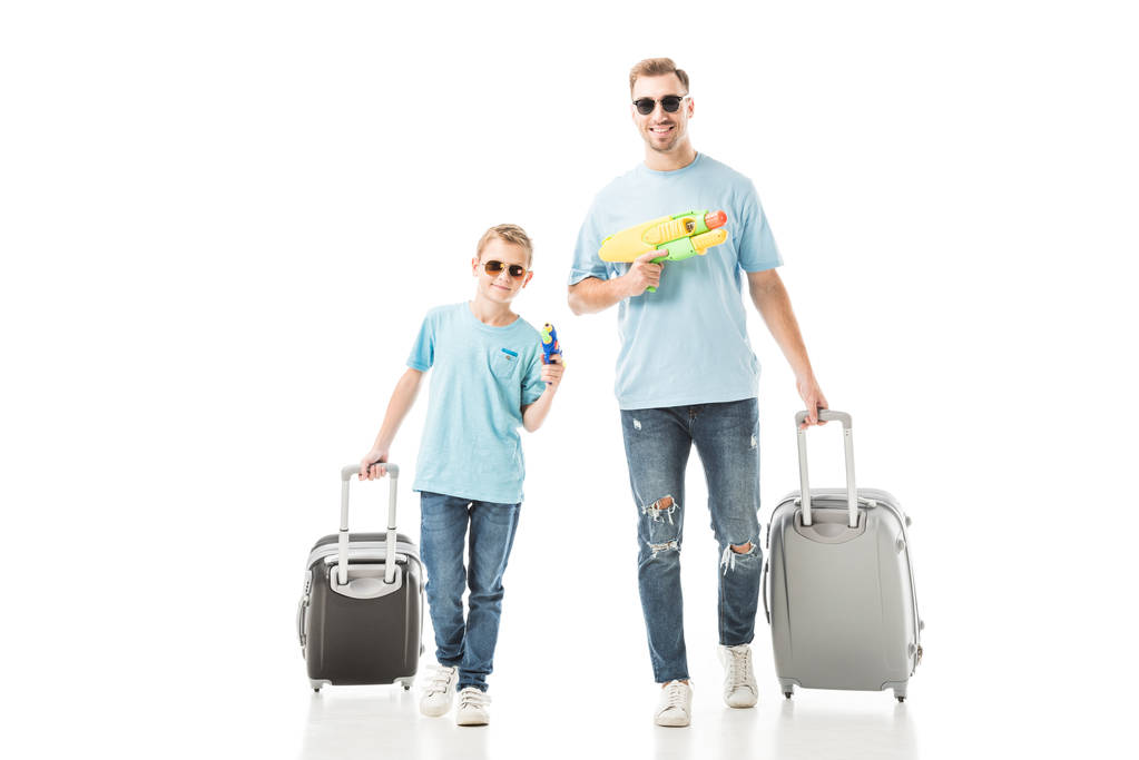 Dad and son walking with luggage and holding water guns isolated on white - Photo, Image