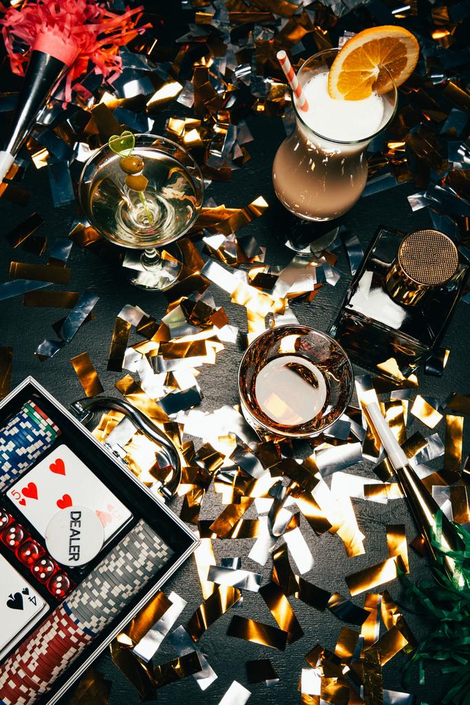 το Top view αλκοολούχα κοκτέιλ, παίζουν χαρτιά, μάρκες πόκερ και κόμμα κέρατα στο τραπέζι που καλύπτονται από χρυσές κομφετί  - Φωτογραφία, εικόνα