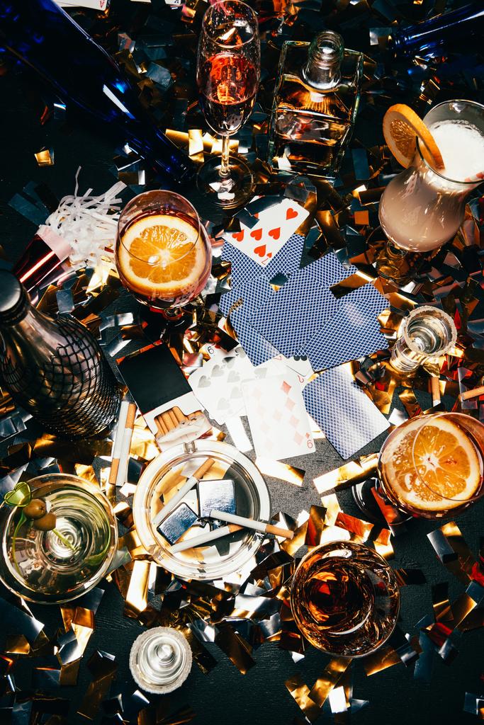 Flach lagen Zigaretten, alkoholische Cocktails, Whiskey und Partyhörner auf einem mit goldenem Konfetti bedeckten Tisch.  - Foto, Bild