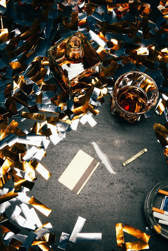 κάτοψη του ουίσκι, έλασης τραπεζογραμματίων, πιστωτική κάρτα και κοκαΐνη στο τραπέζι που καλύπτονται από χρυσές κομφετί  - Φωτογραφία, εικόνα