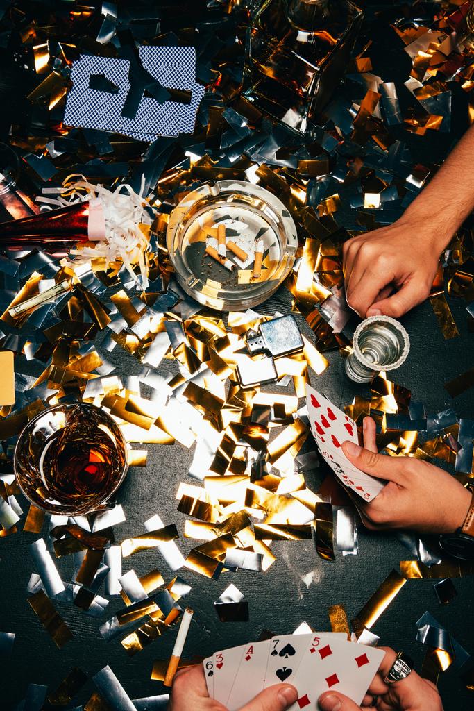 skadrowana przyjaciół płci męskiej, grając w pokera przy stole objęte złotym konfetti - Zdjęcie, obraz