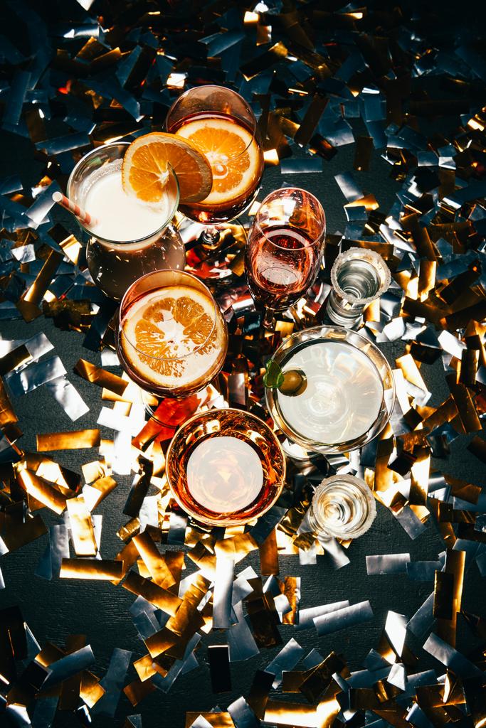 acostado plano con varios cócteles alcohólicos y cuernos de fiesta en la mesa cubierta por confeti dorado
  - Foto, Imagen