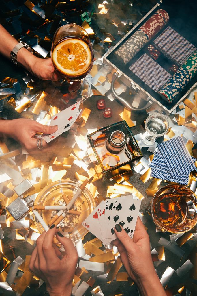 imagen recortada de las mujeres jugando al póquer en la mesa con whisky, cócteles alcohólicos y cigarrillos y confeti dorado
  - Foto, Imagen