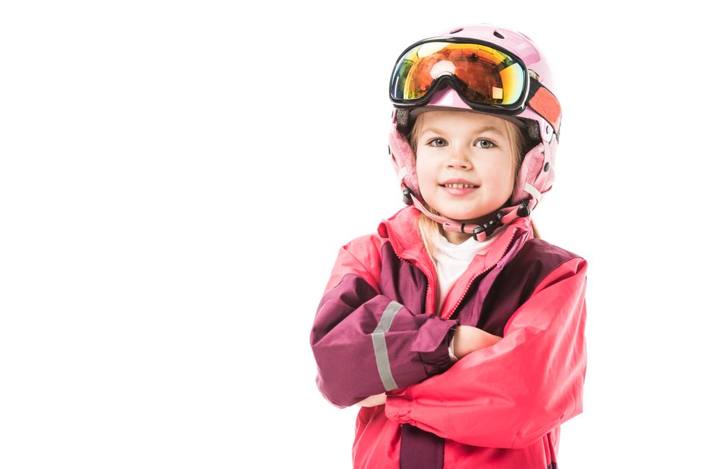 Nettes Vorschulkind in roter Skijacke, Schutzbrille und Helm lächelt und schaut vereinzelt in die Kamera - Foto, Bild