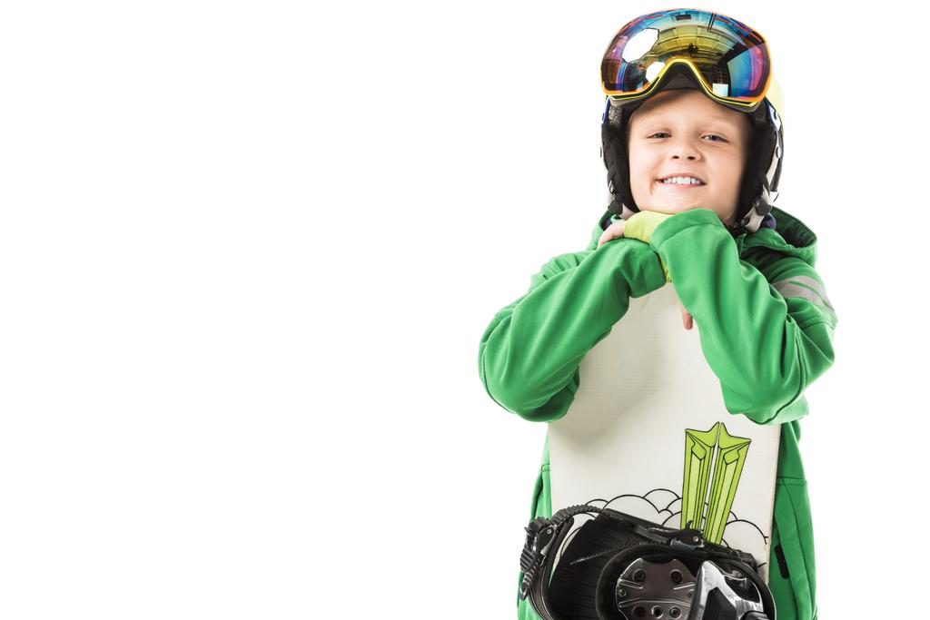 Cute preteen boy in ski suit and goggles leaning on white snowboard, smiling and looking at camera isolated on white - Photo, Image