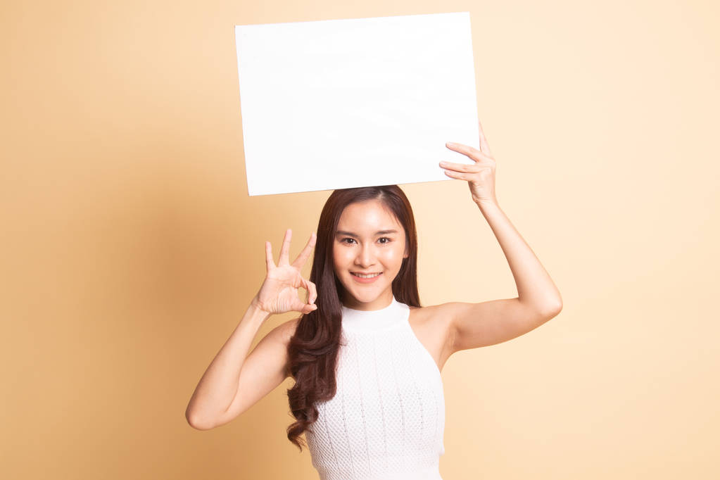Muestra de mujer asiática joven OK con blanco en blanco sobre fondo beige
 - Foto, imagen