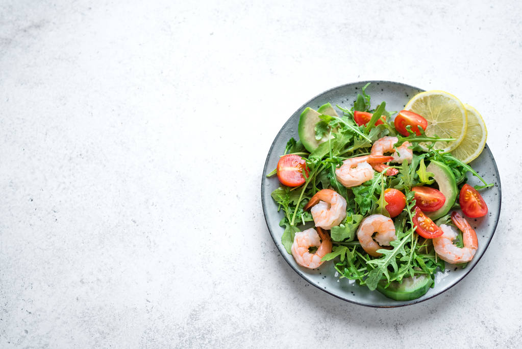 白い石の背景にアボカド海老ルッコラのサラダは、スペースをコピーします。健康的な食事緑エビ (海老)、アボカド、ルッコラ サラダ. - 写真・画像