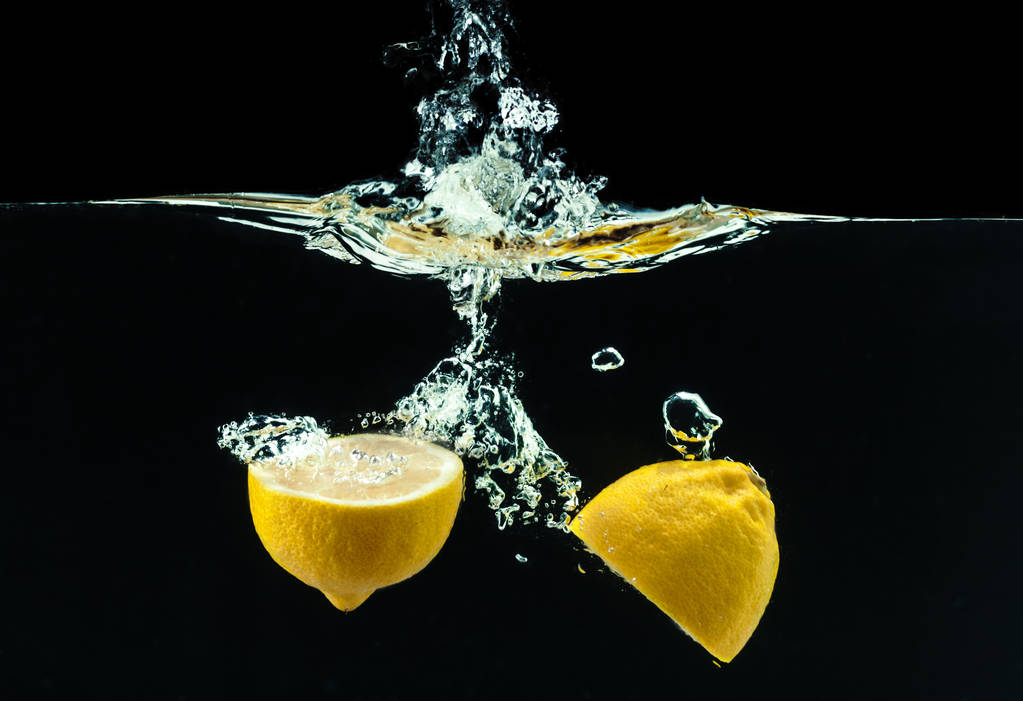 黒い背景に水のしぶきで新鮮な黄色のレモン - 写真・画像