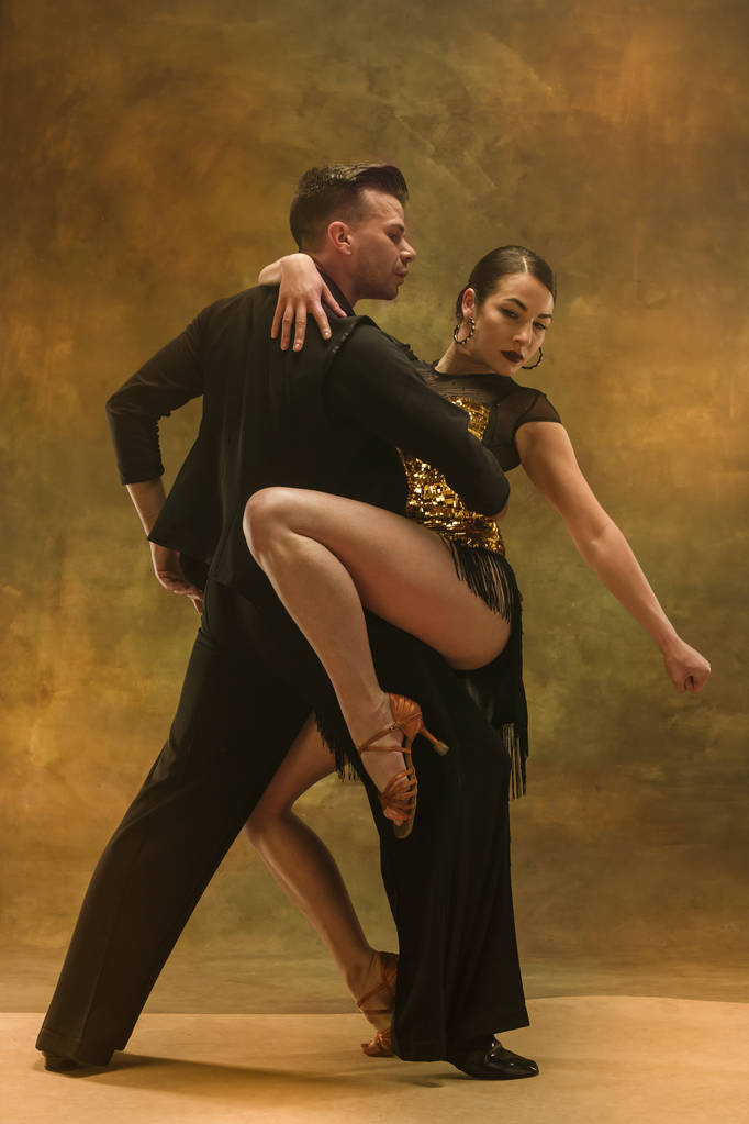 Танцювальна бальна пара в золотій сукні танцює на студійному фоні
. - Фото, зображення