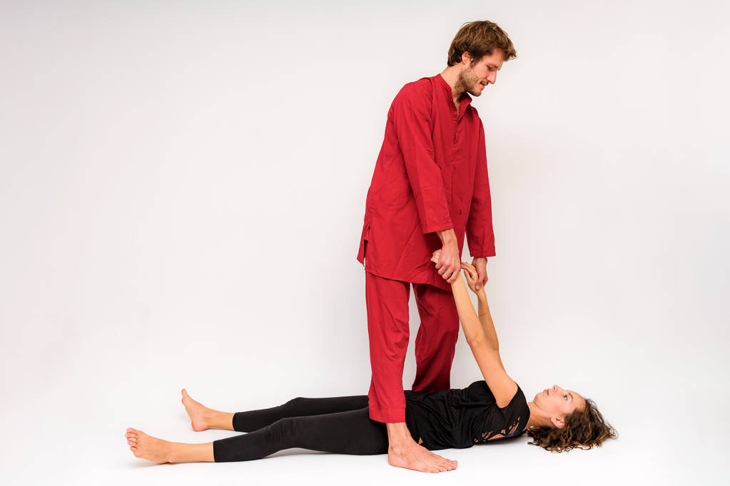 Photo of yoga poses on the floor for two stretching and relaxing on a white background. The man stretches the woman right in front of the camera. - Photo, Image