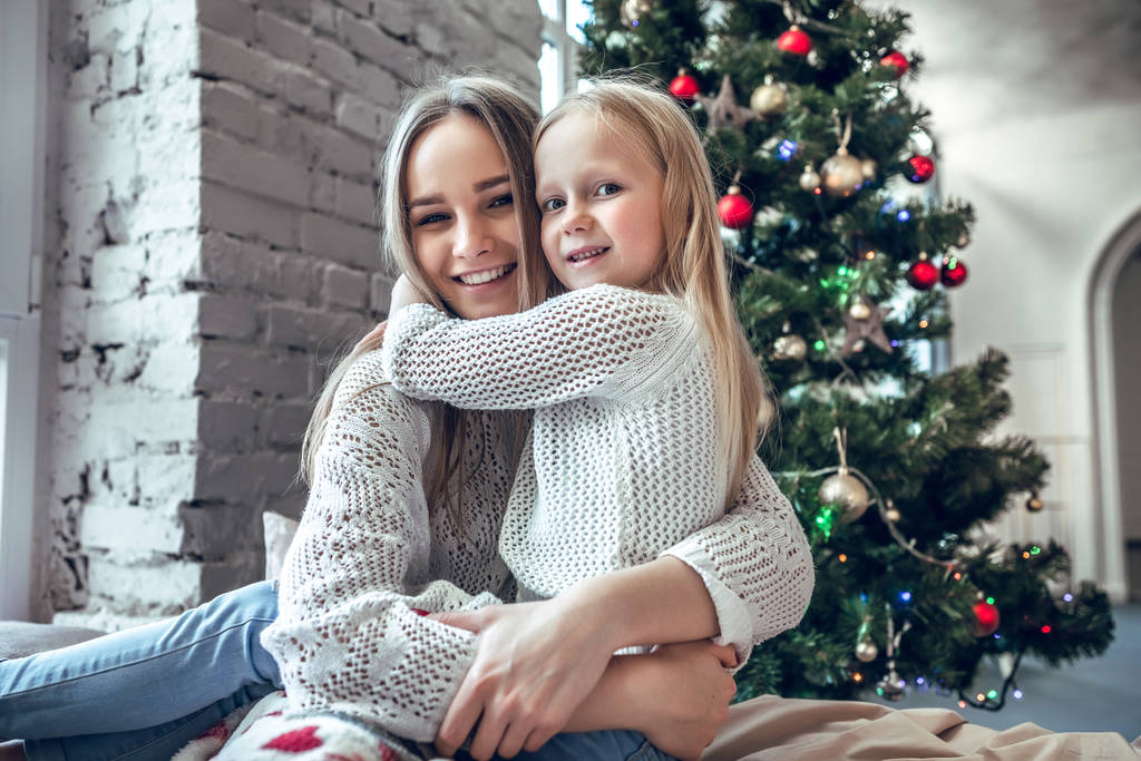 Happy young woman with cute daughter sitting on bed at home, enjoying family, traditional Christmas decoration, New Year holidays concept - Photo, Image