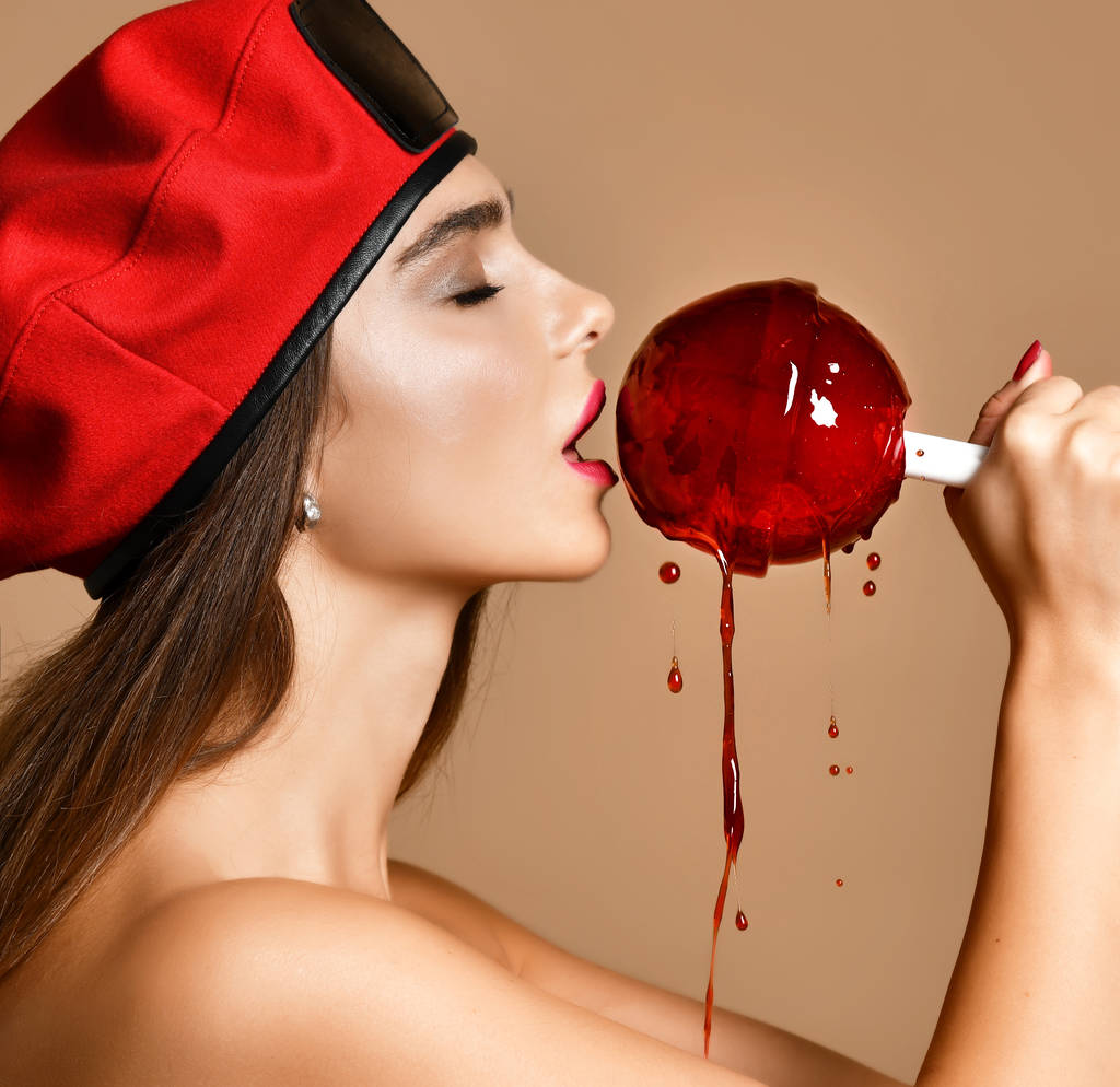 junge brünette Frau mit rotem Baskenmütze lecken riesige rote Lollypop Süßigkeiten mit Spritzern - Foto, Bild