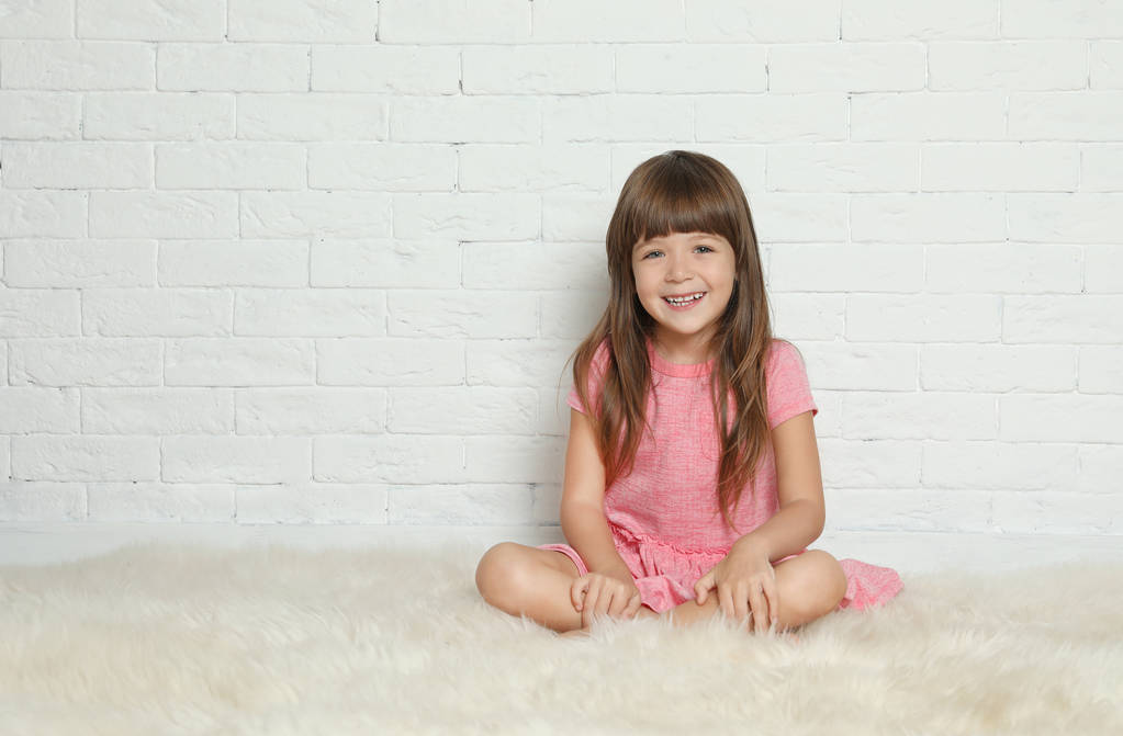 Kürk halı tuğla duvara oturan sevimli küçük kız. Metin için yer - Fotoğraf, Görsel