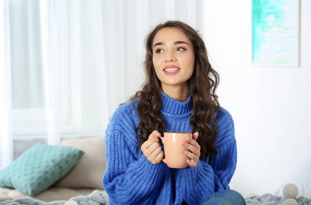 Giovane bella donna in maglione caldo con tazza di bevanda calda a casa
 - Foto, immagini