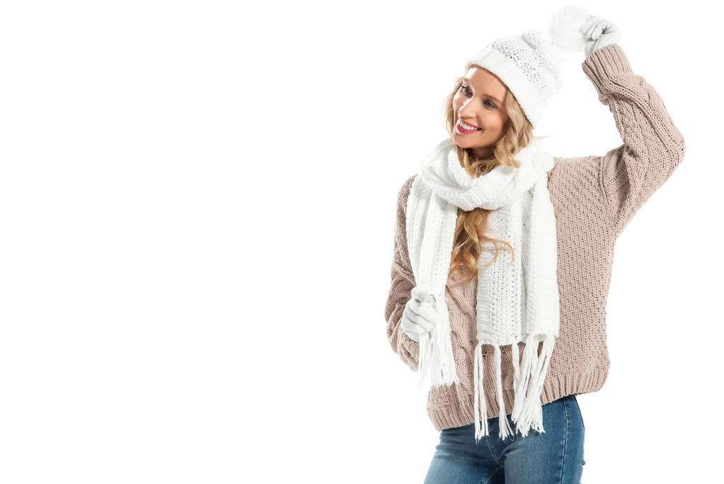 Весела молода жінка в бежевому в'язаному светрі, білому капелюсі, рукавичках і шарфі посміхається ізольовано на білому
 - Фото, зображення