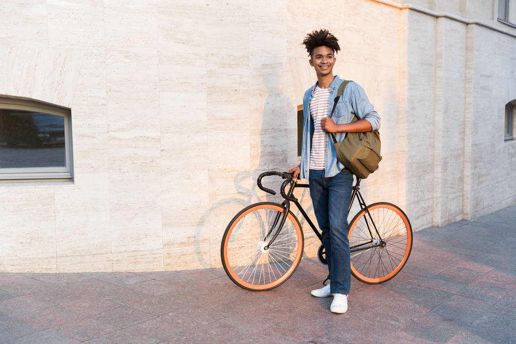 Kuva iloinen nuori afrikkalainen kaveri kävely polkupyörän ulkona kadulla
. - Valokuva, kuva