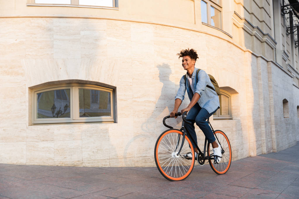 Bild eines glücklichen jungen Afrikaners, der mit dem Fahrrad im Freien auf der Straße läuft. - Foto, Bild