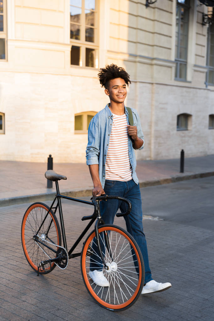 Зображення щасливого молодого африканського хлопця, що йде з велосипедом на вулиці
. - Фото, зображення