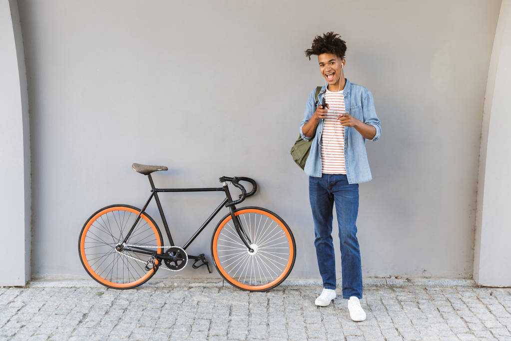 Wizerunek szczęśliwy młody facet Afryki, chodzenie na zewnątrz z rowerów słuchania muzyki, rozmowy przez telefon komórkowy. - Zdjęcie, obraz