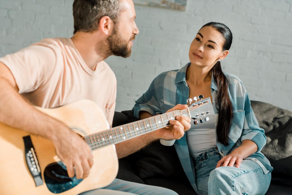 guapo marido tocando la guitarra acústica mientras hermosa esposa escuchándolo
 - Foto, Imagen